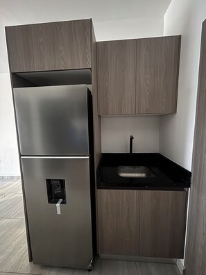 A modern kitchen with a stainless steel refrigerator, wooden cabinets, and a black countertop. - Apartment with comfort, security and exclusivity guaranteed! (Mazatlán)