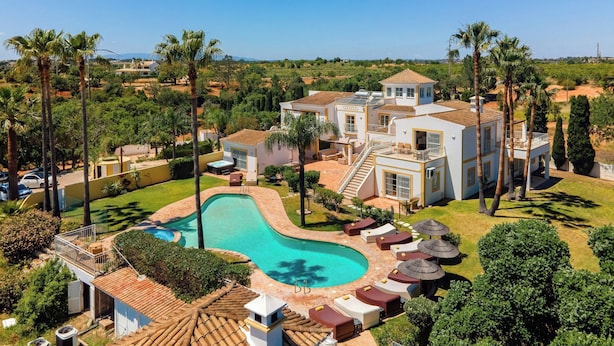Une grande maison avec une piscine, entourée de palmiers et de verdure.