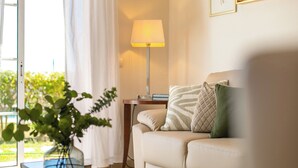 Un salon avec un canapé, une lampe, un vase avec des plantes et une vue sur la verdure à l’extérieur.