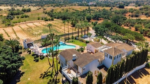 Une grande maison avec une piscine, entourée de palmiers et de vastes champs ouverts.