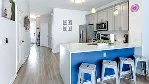 Een moderne keuken met een centraal eiland, barkrukken en roestvrijstalen apparatuur.