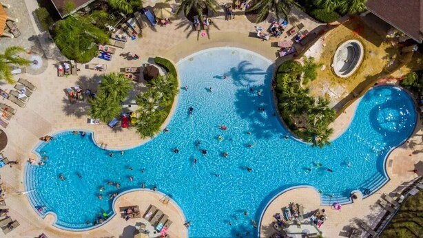 Luchtbeeld van een resort met een groot centraal zwembad, omringd door palmbomen en ligbedden.