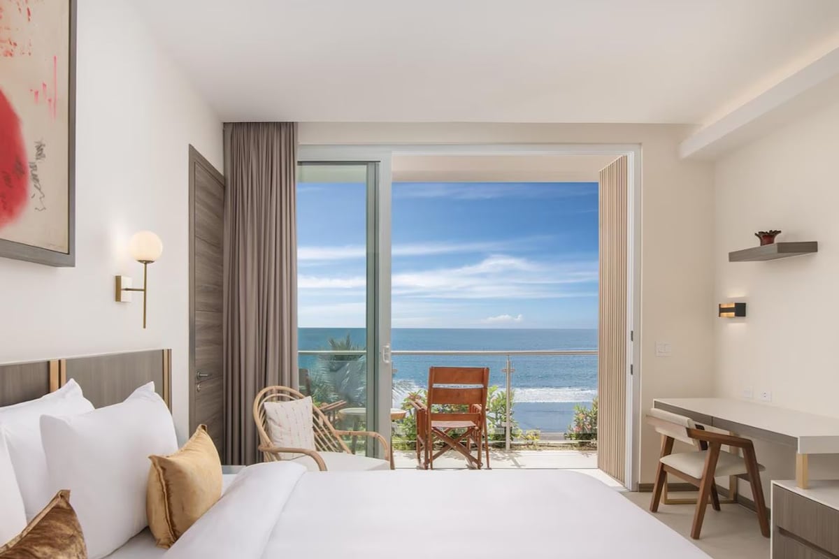 A hotel room with a bed, a desk, a chair, and a view of the ocean.