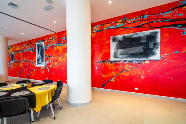 Un espace repas avec des tables dressées pour le service, une grande colonne et des œuvres d’art murales abstraites aux couleurs vives.