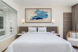 Habitación de hotel moderna con una cama grande, cabina de ducha de vidrio, un cuadro abstracto colgado en la pared y un armario de madera.