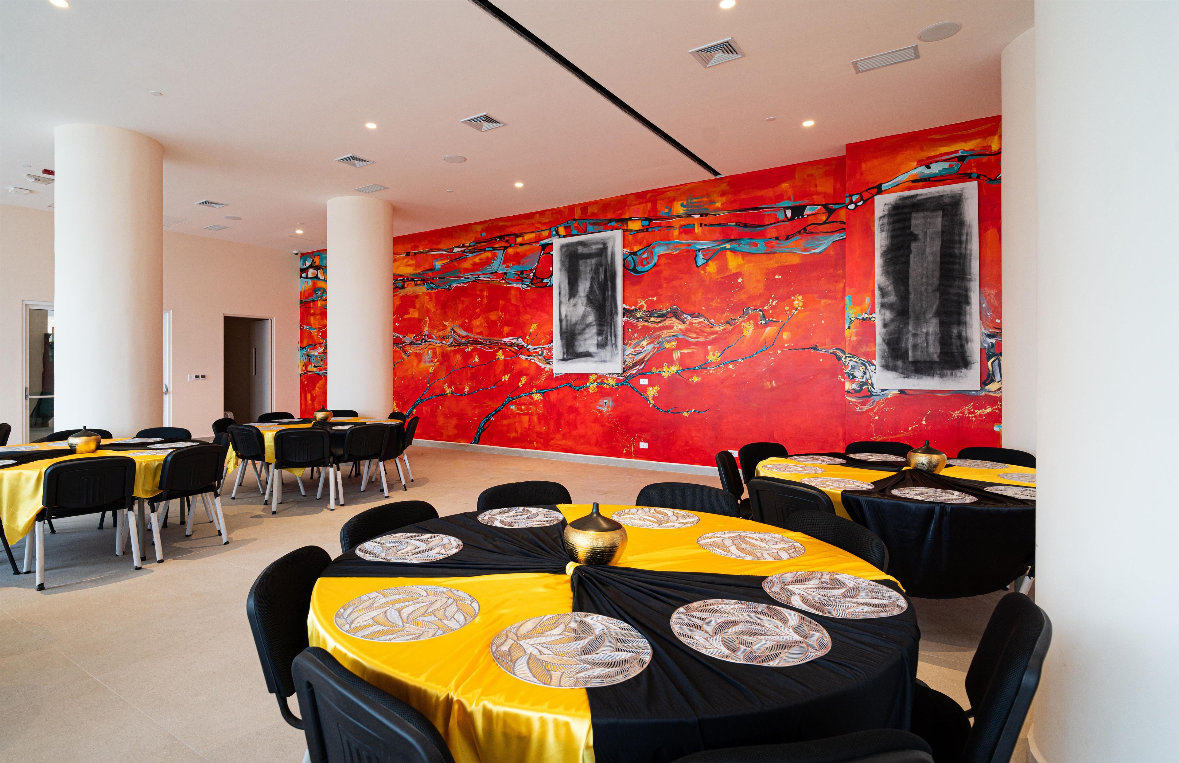 A conference room with round tables, black and yellow tablecloths, and a vibrant abstract mural on the wall.