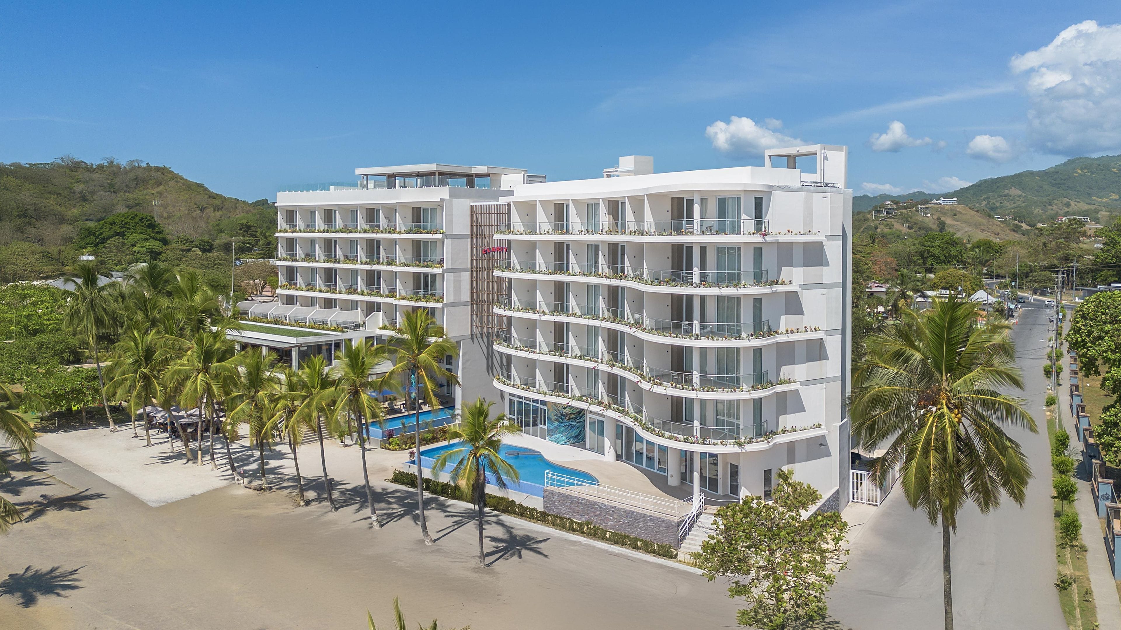 A multi-story hotel with balconies, a swimming pool, and palm trees.
