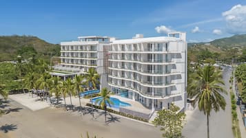A multi-story hotel with balconies, a swimming pool, and palm trees.