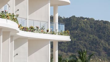 A multi-story hotel with balconies, each adorned with plants and offering views of a forested hillside.