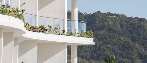 Un hôtel à plusieurs étages doté de balcons, chacun agrémenté de plantes et offrant une vue sur une colline boisée.