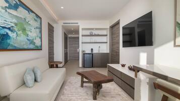 A modern living room with a sofa, a wooden coffee table, and a kitchen area with a fridge and shelves.
