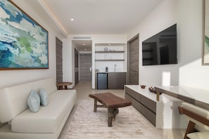 A modern living room with a sofa, a wooden coffee table, and a kitchen area with a fridge and shelves. - Clarita's Beach Bar & Resort, WorldHotels Elite (Jacó)