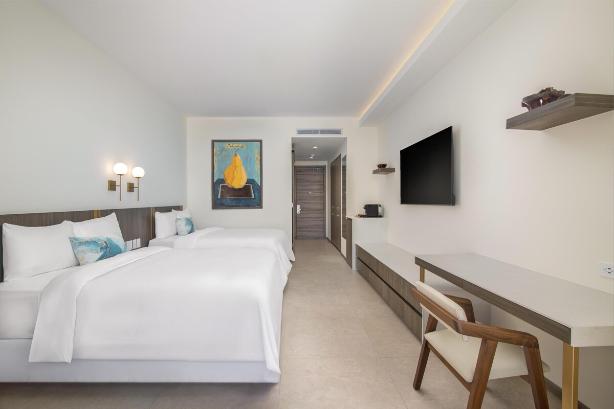 Habitación de hotel con una cama grande, un escritorio, una silla, un televisor y un cuadro en la pared.