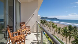 Un balcon avec vue sur la plage, les palmiers et une montagne au loin.