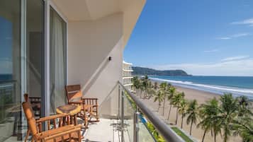 Un balcón con vista a la playa, palmeras y una montaña a lo lejos.