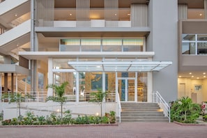 Un hotel de varios pisos con un atrio central, barandillas de vidrio y una escalera que conduce a la entrada.