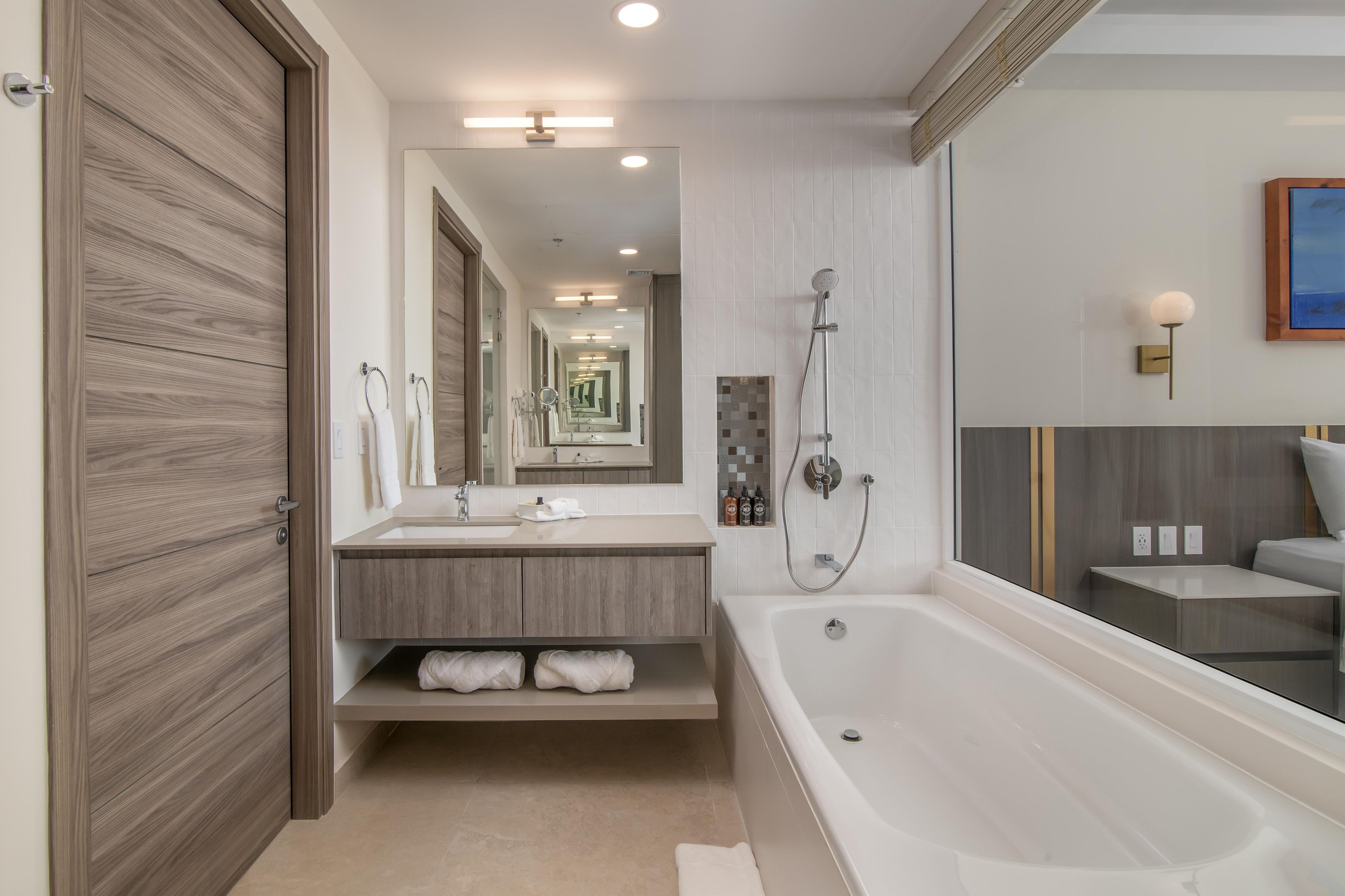Une salle de bain moderne dotée d’une grande baignoire, d’un meuble-lavabo avec miroir et d’un espace douche.