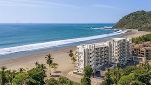 Un hôtel situé sur la côte, composé de plusieurs bâtiments, avec une plage et une colline boisée.