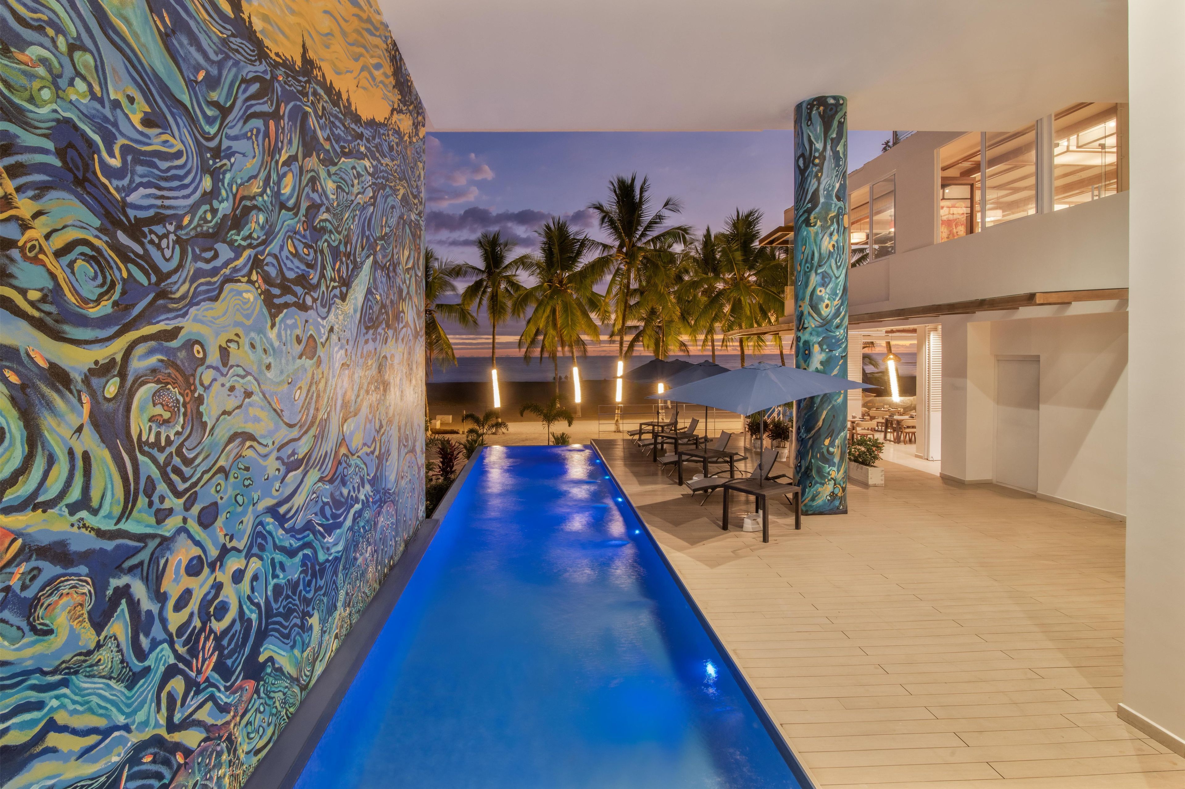 A pool with a blue water feature, palm trees, and a modern building with large windows.