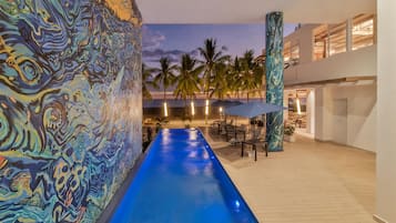 A pool with a blue water feature, palm trees, and a modern building with large windows.