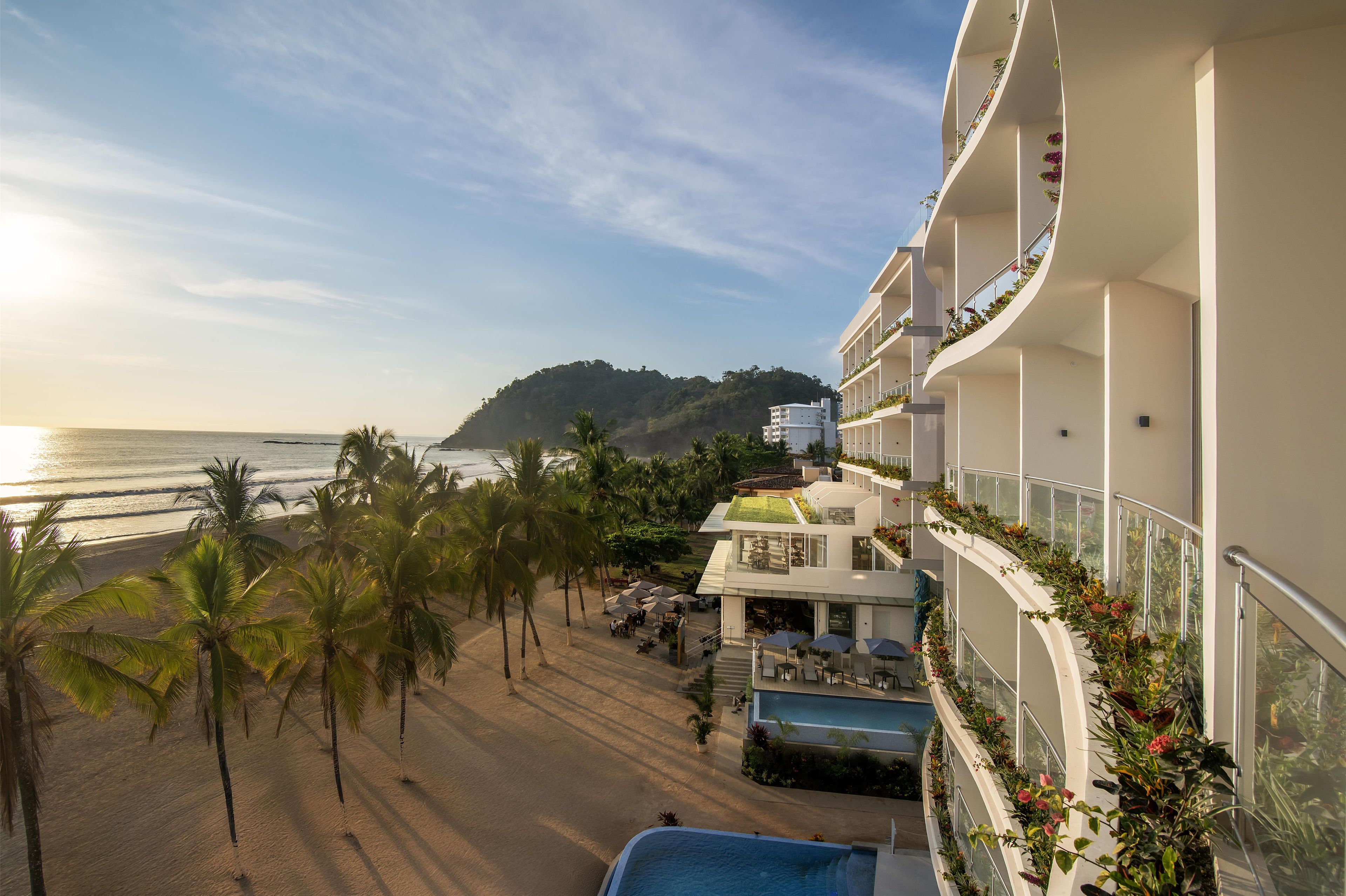A hotel with a pool, beach view, and balconies with plants.