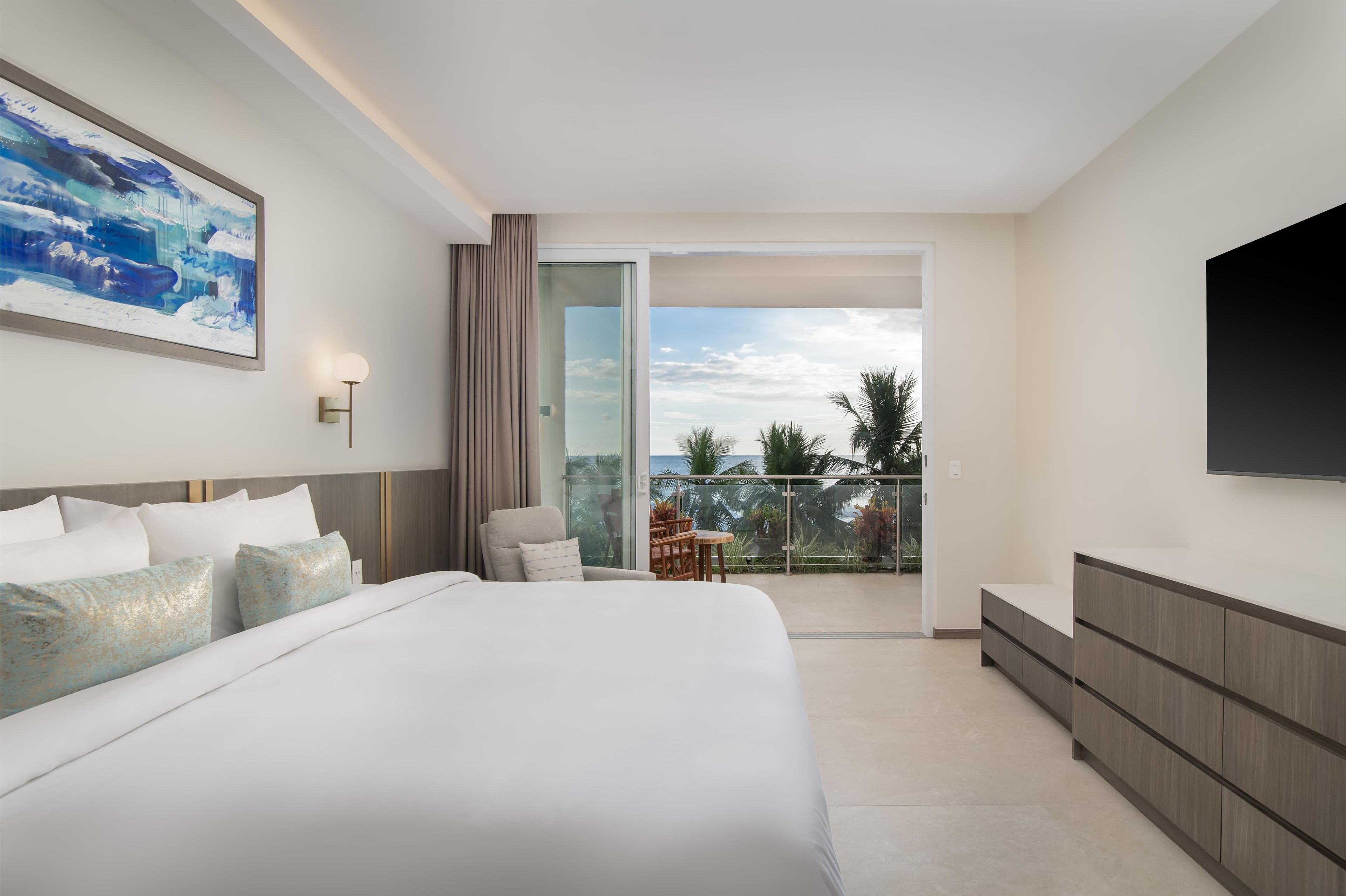 Een moderne hotelkamer met een groot bed, een flatscreen-tv, een balkon met uitzicht en een zithoek.