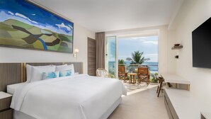 Une chambre d’hôtel avec un grand lit, un tableau, une télévision et un balcon avec des chaises.