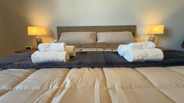 A neatly made bed with a dark headboard, two bedside lamps, and rolled towels on the bed. - Harmony Home Florence (Firenze)