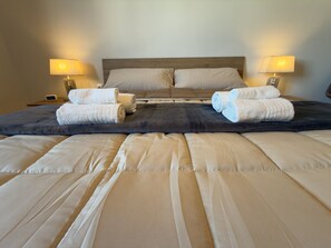 A neatly made bed with a dark headboard, two bedside lamps, and rolled towels on the bed. - Harmony Home Florence (Firenze)