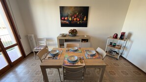 A dining area with a wooden table set for four, chairs, a painting of fruits on the wall, and a coffee machine on a shelf. - Harmony Home Florence (Firenze)