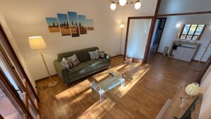 A spacious living area with a wooden floor, a green sofa with patterned cushions, a glass coffee table, and a modern pendant light. - Harmony Home Florence (Firenze)