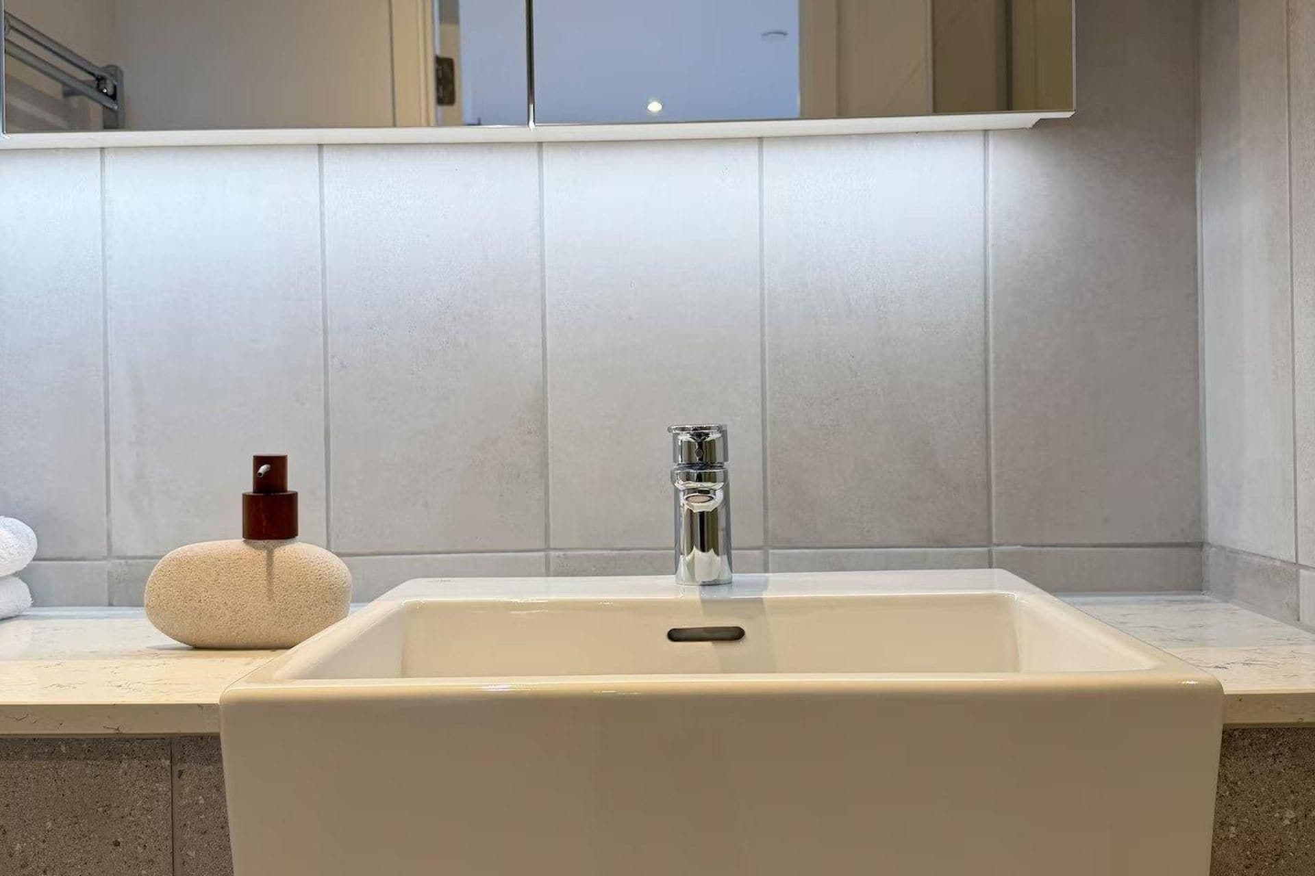 Une salle de bain avec un lavabo blanc, un miroir au-dessus et un porte-serviettes à gauche.