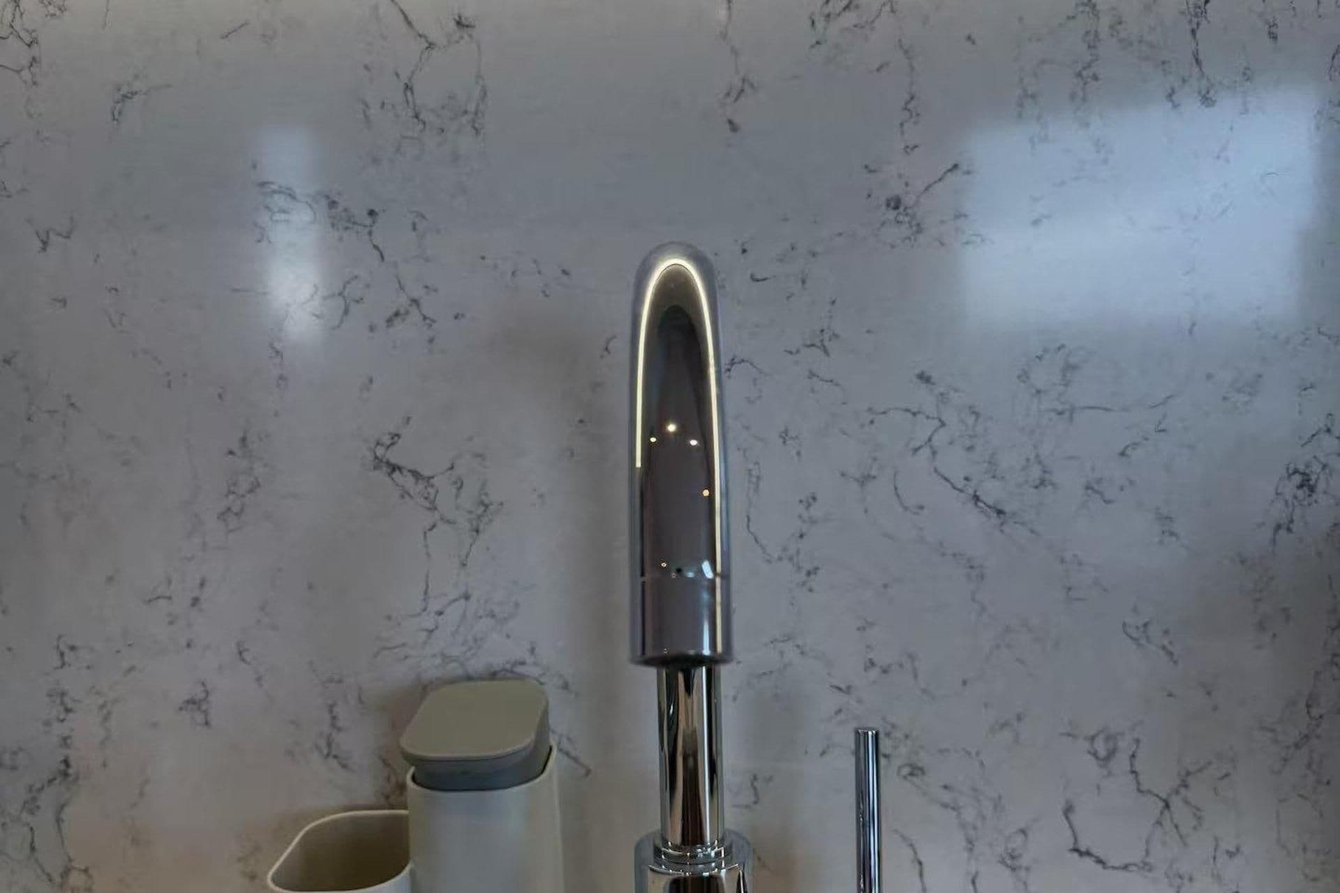 A modern bathroom with a marble backsplash, a chrome faucet, and a small trash bin.