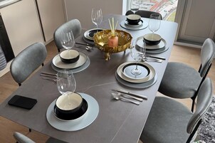 Una mesa de comedor dispuesta con platos, tazones, cubiertos y vasos, con un cuenco decorativo y una botella de agua.