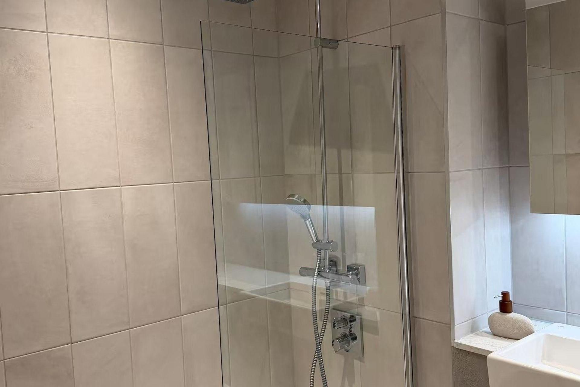 Une salle de bain moderne avec une douche à parois de verre, un lavabo blanc et un grand miroir.