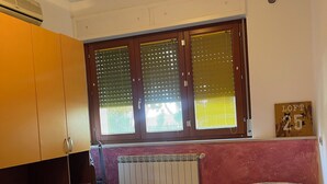 Une chambre avec deux lits simples, un radiateur, une fenêtre avec des stores et une enseigne indiquant qu’il s’agit d’un appartement mansardé.