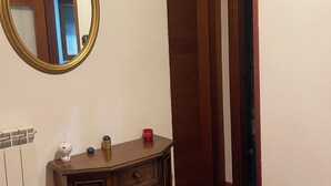 Une chambre d’angle avec une commode en bois, un miroir rond et une porte donnant sur une autre pièce.
