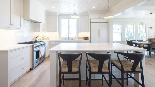 Una cocina moderna con armarios blancos, una isla grande con taburetes y lámparas colgantes.