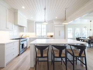 A modern kitchen with white cabinetry, a large island with bar stools, and pendant lighting. - 4BR Coastal Home w/ Rooftop Deck | Sleeps 12! (Cape May)
