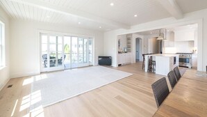 Un amplio salón con piso de madera, una mesa de comedor y una cocina con gabinetes blancos y estufa.