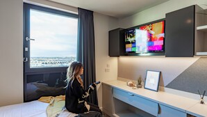 Hotelkamer met een bed, een aan de muur bevestigde televisie, een bureau en een raam met uitzicht op de stad.