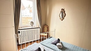 Een slaapkamer met twee bedden, een raam met gordijnen, een radiator en een spiegel aan de muur.
