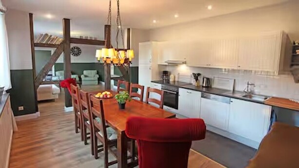 Een moderne keuken met witte kasten, een houten eettafel en een rode stoel.