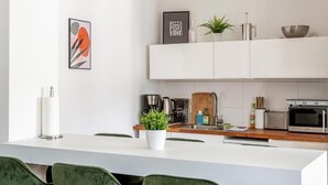 A modern kitchen with white cabinetry, a central island, green chairs, and a potted plant. - Global Living Moritzplatz (Berlin)