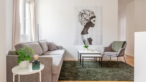 A modern living room with a grey sofa, a small round table with a plant, a green rug, and a wall-mounted artwork. - Global Living Moritzplatz (Berlin)