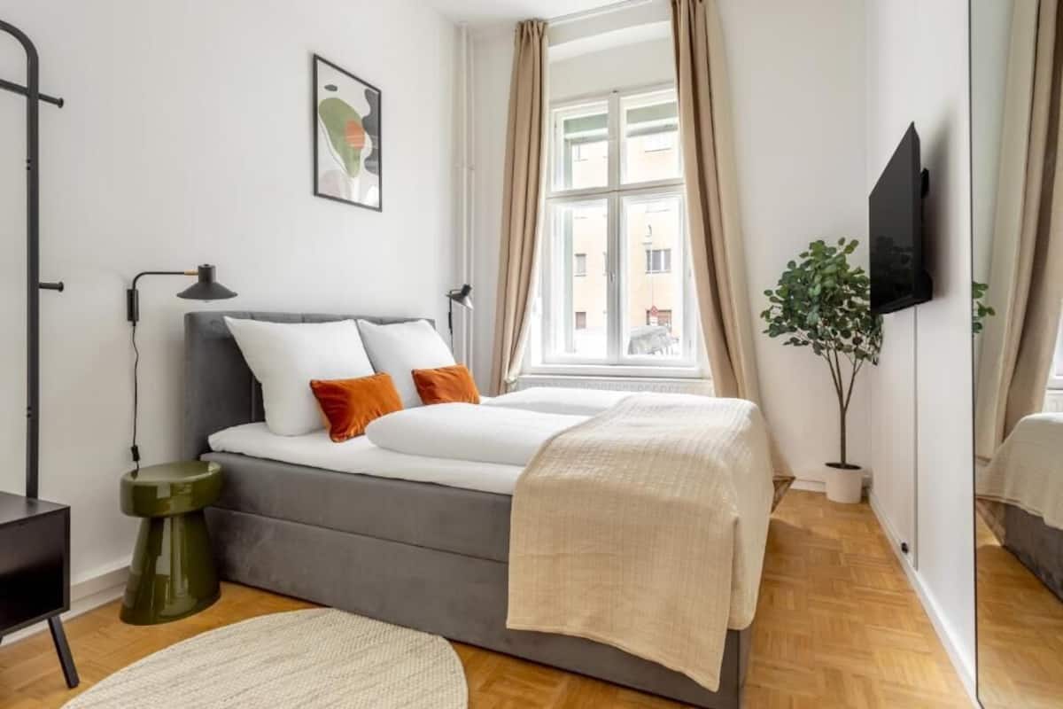 Ein modernes Schlafzimmer mit einem Bett, Nachttischen, einem Fernseher und einem Fenster mit Vorhängen.