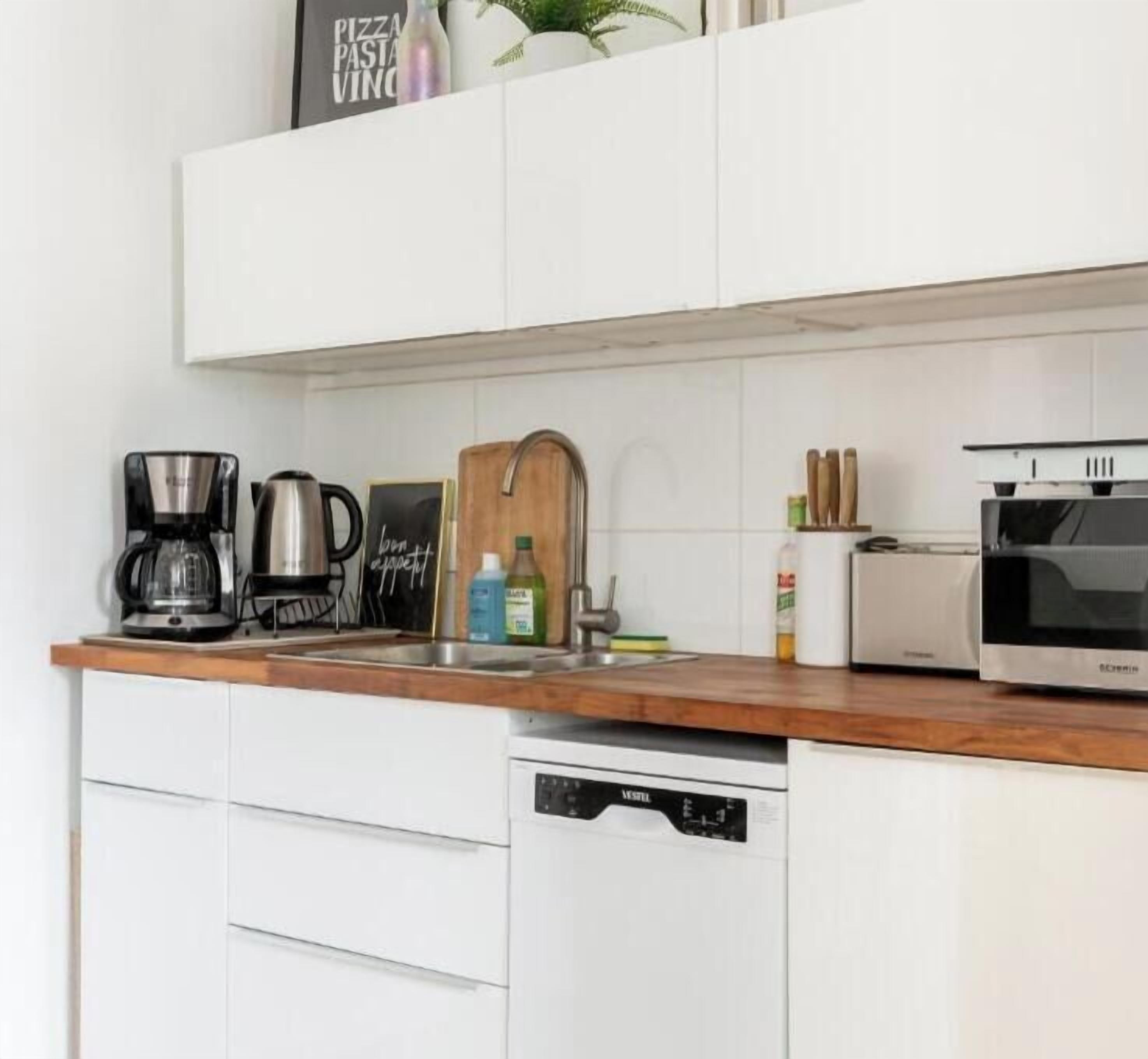 A modern kitchen with white cabinets, a wooden countertop, a coffee maker, a toaster, a microwave, and a dishwasher.