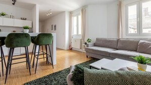 A modern living room with a grey sofa, two green chairs, a white coffee table, and a black rug. - Global Living Moritzplatz (Berlin)