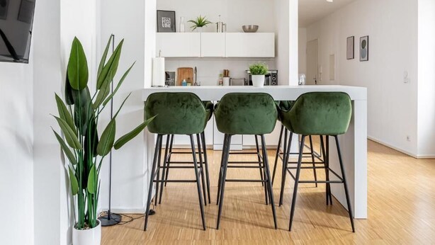 A modern kitchen with a central island, three green bar stools, and a potted plant. - Global Living Moritzplatz (Berlin)