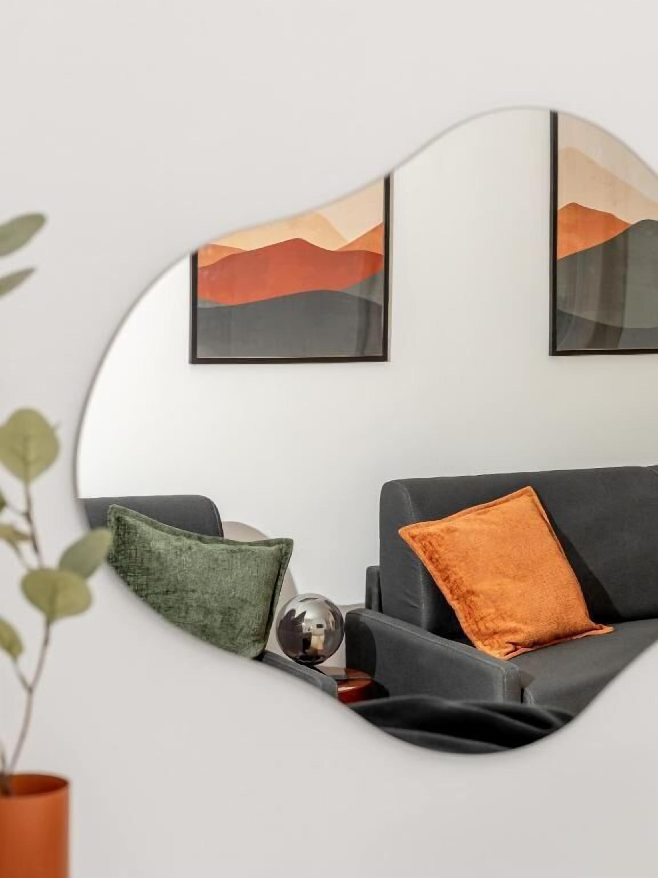 Ett modernt vardagsrum med en grå soffa, en grön kudde och en orange kudde. På väggen hänger två inramade abstrakta tavlor.